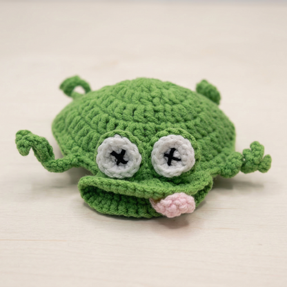 Green crochet toy with googly eyes and a pink nose on a light background