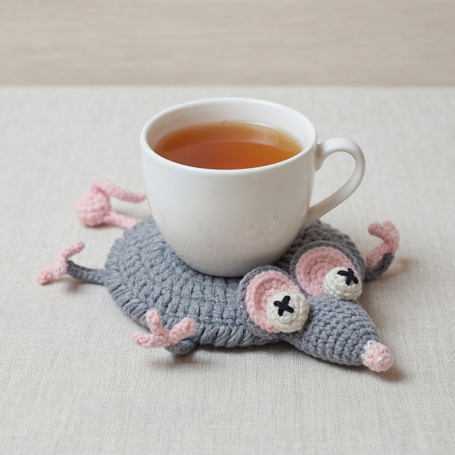 Mouse-shaped crocheted coaster with a cup of tea on a light surface
